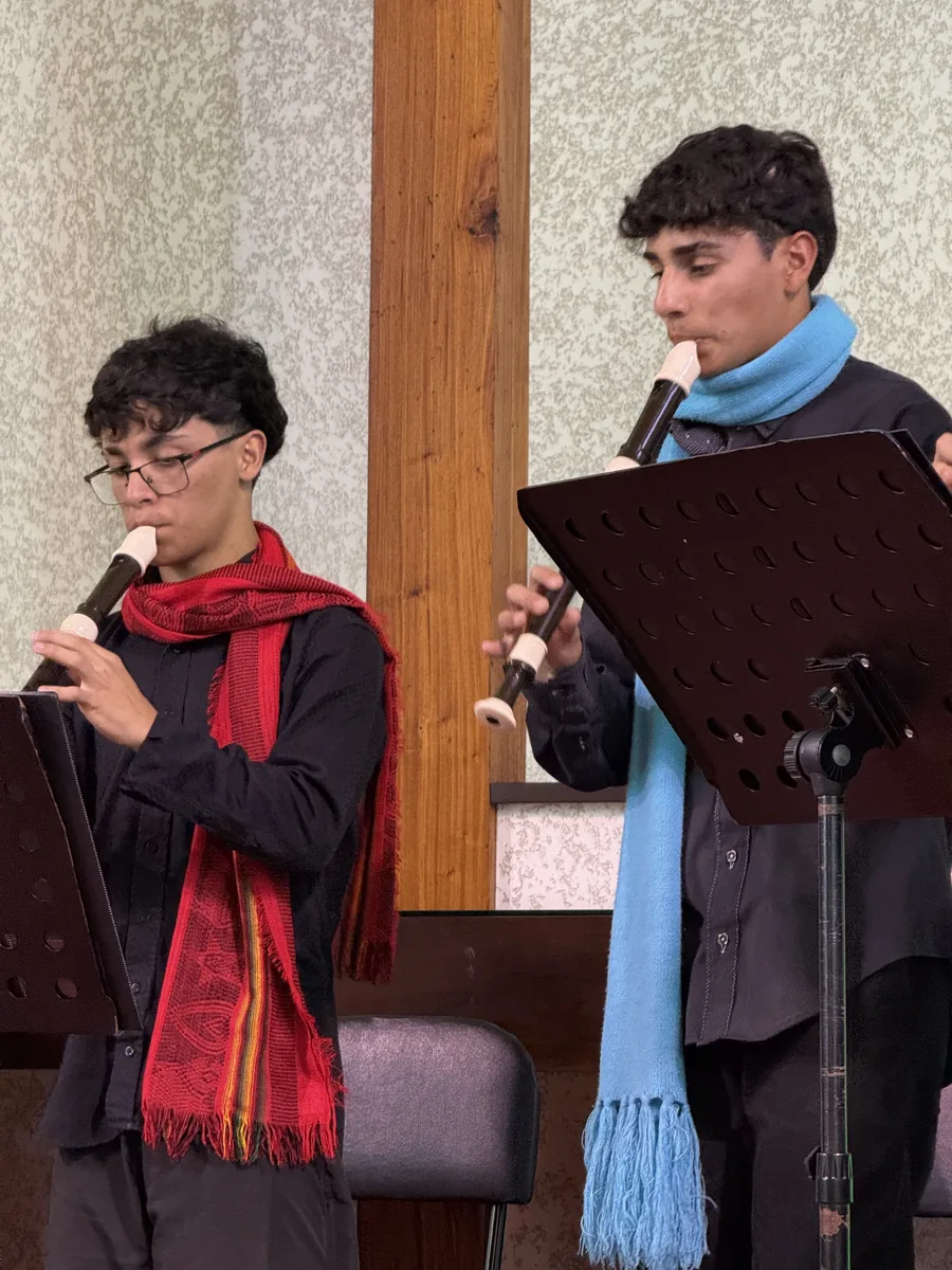 Dois integrantes tocando flauta doce diante da estante de partituras